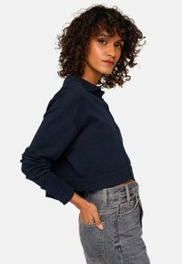 Pull cropped bleu marine en tissu doux, avec un devant à boutons, un col et des manches longues. Assorti à un jean gris taille haute.