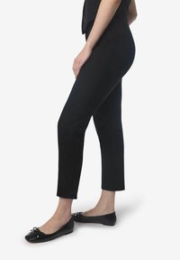 Pantalones negros de longitud tobillo, fabricados en un tejido suave con un ajuste entallado; presentan un diseño limpio sin patrones ni acentos visibles.