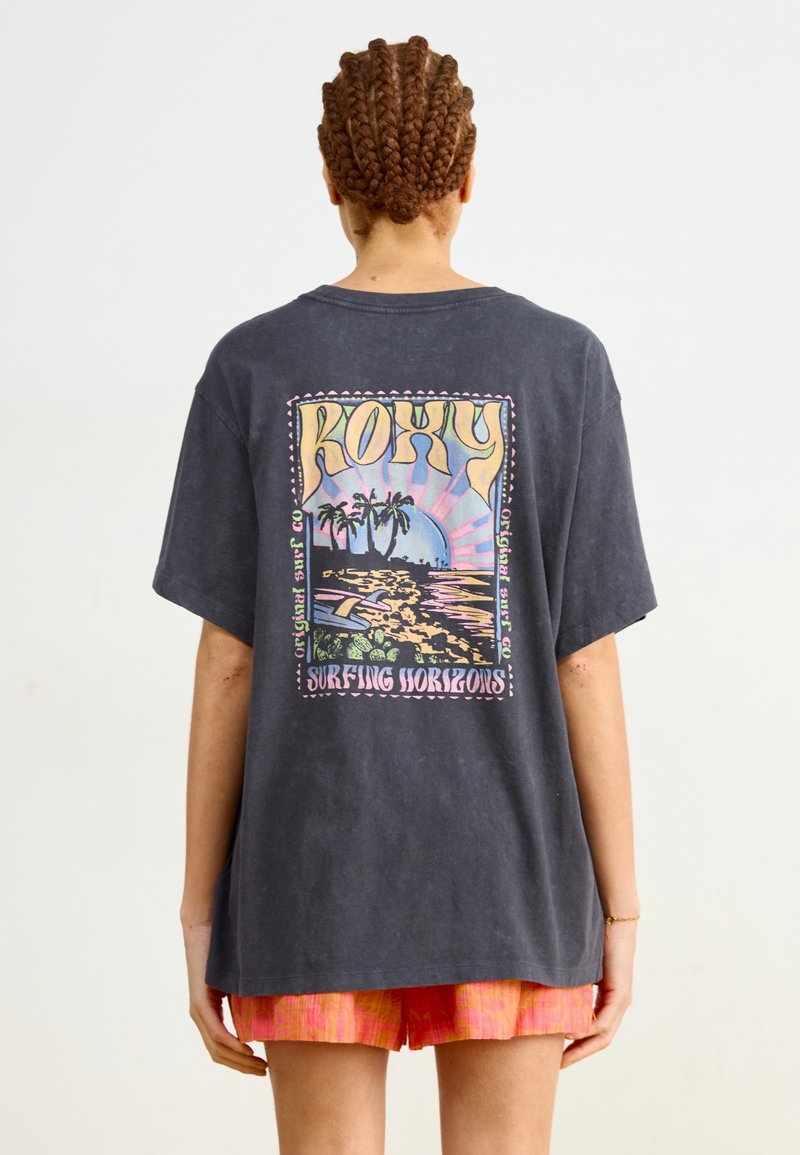 Svart oversized T-skjorte med et fargerikt grafisk design med palmer, bølger og teksten "ROXY SURFING HORIZONS" i retro stil på baksiden.