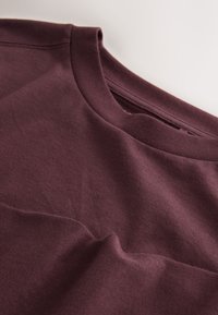 Bordó pamut póló lekerekített nyakkivágással és finom textúrával, sima felülettel és minimális varrási részletekkel.