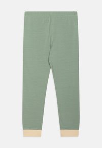 Leggings de color verde claro con una textura suave, que presentan un corte holgado y puños de color crema en los tobillos. Cintura elástica para mayor comodidad.