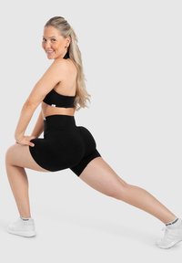Top sportivo nero e pantaloncini a vita alta in un tessuto morbido, caratterizzati da una vestibilità aderente e cuciture piatte, abbinati a scarpe da ginnastica bianche.