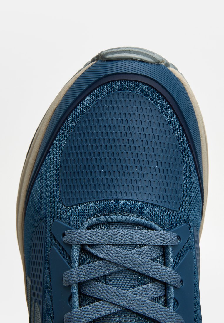Scarpa sportiva blu con tomaia in mesh testurizzato, punta rinforzata, lacci piatti e suola in gomma beige. Forma leggermente arrotondata.
