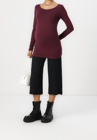Top de manga larga color granate con escote redondo, combinado con culottes negros acanalados, botas de combate negras con cordones y un bolso blanco.