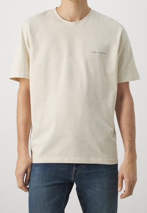 Beige cotton t-shirt with short sleeves and a crew neck. Features a small black text logo "TIGER OF SWEDEN" on the left side.