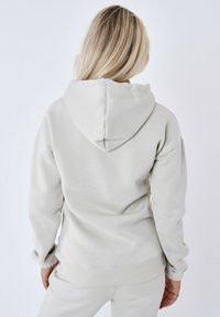 Lichtgrijze hoodie met een zachte textuur, voorzien van een trekkoordkap, geribde manchetten en een relaxte pasvorm. Van achteren weergegeven.