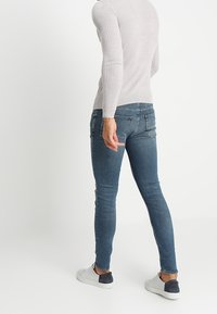 Smalblå jeans med en blekt finish, kombinerade med en ljusgrå ribbstickad långärmad topp och vita sneakers med mörka detaljer.