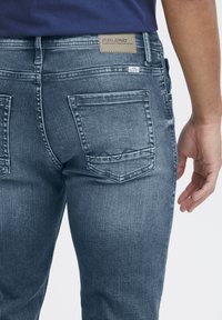 Slim-fit blå denimjeans med en stone-washed textur, som har två bakfickor och en märkesetikett sydd på midjebandet.