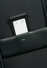 Black luggage tag holder with a textured surface, featuring a white information card for name, phone, email, and address. Blue accent stitch visible.