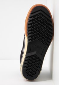 Černá plátěná skate bota s gumovou podrážkou, která má diamantový vzor a logo Vans, a gumový kryt špičky.