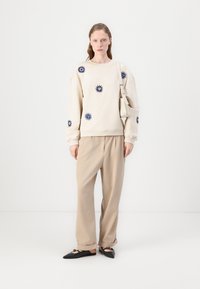 Beige sweatshirt med marinblå blommönsterbroderi, kombinerad med lösa beige byxor och svarta spetsiga ballerinas. Axelremsväskan fulländar outfiten.