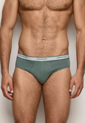 Grüne Baumwollslips mit einem grauen Bund, auf dem "yamamay" gedruckt ist. Der Stoff wirkt weich; das Design umfasst eine figurbetonte Passform und einen Standardschnitt.