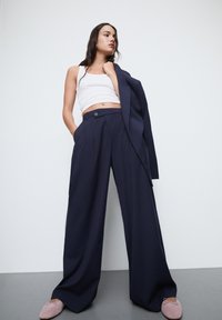 Navy pinstripe leveät lahkeet korkealla vyötäröllä, yhdistetty valkoiseen lyhythihaiseen toppiin ja pehmeisiin vaaleanpunaisiin tasapohjaisiin kenkiin.