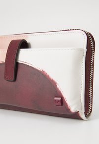 Geldbörse mit einem rosa und weißen Stoffaußenmaterial und einem weinroten Spritzdesign, mit Reißverschluss und einem kleinen geprägten Logo an der Seite.