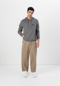 Sweatshirt cinza com capuz e bolso frontal, combinado com calças largas bege e ténis brancos. Design simples e ajuste descontraído.