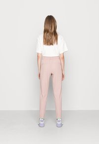 Ljust rosa byxor med avslappnad passform, elastisk midja och två bakfickor, kombinerat med vit skjorta och flerfärgade sneakers.
