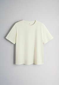 Plain short-sleeve white crewneck t-shirt hanging on a light gray wall background.
