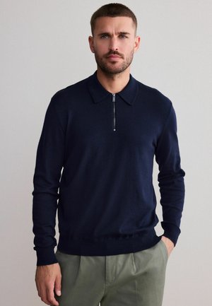 Suéter navy con cuello con cremallera, mangas largas y dobladillo acanalado. Fabricado con un material suave y un diseño ajustado.