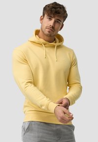 Gul hoodie med snore, ribbede manchetter og et lille grafisk logo. Blødt stof med en afslappet pasform, parret med grå bukser.