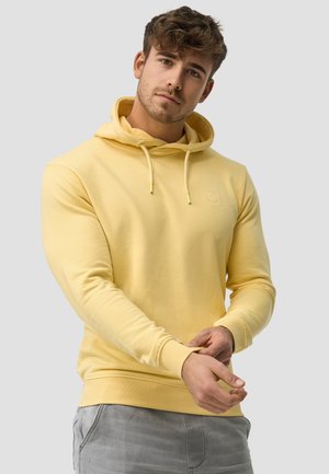 Gul hoodie med snore, ribbede manchetter og et lille grafisk logo. Blødt stof med en afslappet pasform, parret med grå bukser.