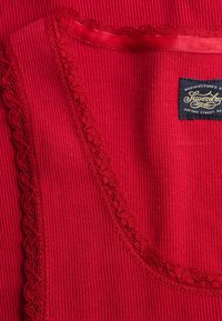 Tissu rouge à côtes avec bordure en dentelle festonnée et une étiquette rectangulaire noire cousue dans le coin supérieur droit.