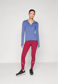 Light blue zip-up athletic jacket with long sleeves paired with high-waisted burgundy leggings featuring mesh detailing, worn with black sneakers.