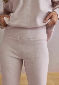 Jasnoróżowy komplet wypoczynkowy z miękkiej, teksturowanej tkaniny. Górna część ma luźny krój, a spodnie mają wysoki stan i smukłą sylwetkę.