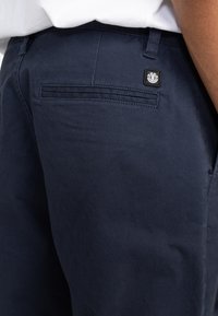 Navy blue cotton pants with a smooth texture, featuring a back pocket and a small black brand label. Simple design with no visible patterns.