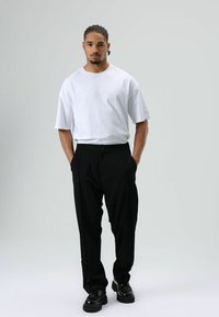 Wit T-shirt met korte mouwen, gecombineerd met zwart op maat gemaakte broek en zwarte schoenen. De outfit heeft een ontspannen pasvorm en een minimalistisch design.