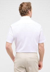 Korte mouwen witte shirt van soepele stof, met een kraag, gestikte details en een casual pasvorm, gecombineerd met beige broeken.