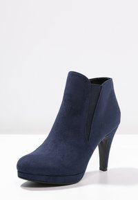 Marinblå ankelstövlar i mocka med en elegant design, rund tå och en glänsande svart klack, med elastiska sidopaneler för enkel påklädning.