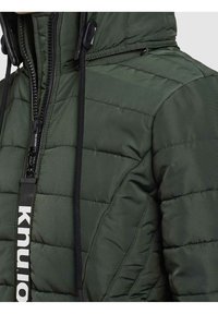 Ciemnozielona kurtka ocieplana o pikowanym wzorze, z frontowym zamkiem błyskawicznym, regulowanym kapturem i kontrastowym logo na uchwycie zamka.