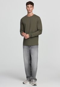 T-shirt in cotone verde oliva a maniche lunghe abbinato a jeans denim grigio chiaro e sneakers grigie, con una vestibilità comoda e scollo rotondo.