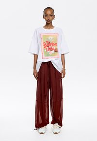 Camiseta blanca de gran tamaño con un gráfico floral colorido. Pantalones burdeos fluidos con cinturón atado. Zapatillas casuales blancas y azules.