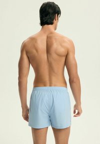 Jasnoniebieskie szorty kąpielowe z elastycznym paskiem w talii i bocznymi kieszeniami, widok z tyłu. Materiał wydaje się lekki i gładki.