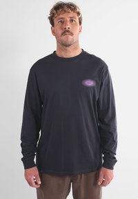 T-shirt noir à manches longues en coton, avec un design graphique violet sur la poitrine. Col rond avec des poignets et un ourlet côtelés.
