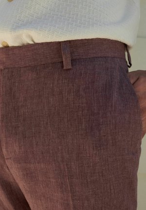 Bordó lněné kalhoty s texturovanou tkaninou, rovný střih a kapsami po stranách, v kombinaci s bílou košilí se vzorem a knoflíkovými detaily.