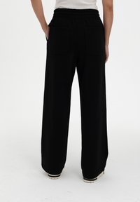 Black wide-leg trousers with an elastic waistband, featuring two back pockets and a smooth fabric texture.