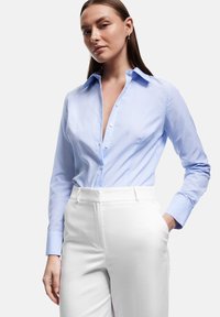 Lyseblå og hvidstribet skjorte med knapper, krave, lange ærmer og slim fit, parret med højtaljede hvide bukser.