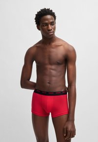 Red cotton boxer briefs with a black waistband featuring "HUGO" logo. The design is fitted with a smooth texture and short legs.