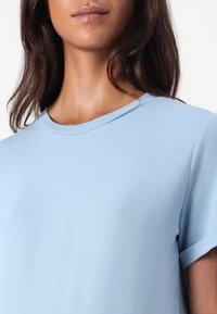 Tricou din bumbac de culoare albastru deschis, cu gât rotund, mâneci scurte și textură netedă. Prezintă un design curat și simplu, fără modele sau accente.