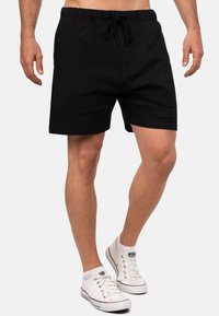 Zwarte katoenmix korte broek met een elastische tailleband en trekkoord, voorzien van zijzakken en een gladde textuur. Gecombineerd met witte sneakers.