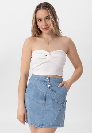 Crop top blanc à côtes avec un détail torsadé, associé à une jupe en denim bleu clair avec un design asymétrique et des boutons argentés.