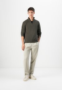 Maglione a coste di un verde scuro con collo zip, abbinato a pantaloni tapered color beige chiaro e sneakers crema. Design minimalista, tessuto morbido.
