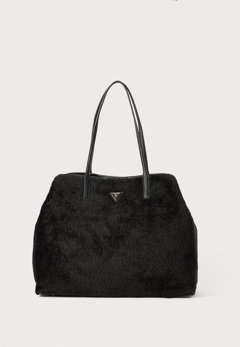 Sac fourre-tout noir duveteux avec longues lanières en cuir et un petit logo triangulaire en métal de la marque au centre à l'avant.
