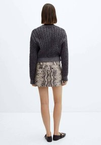Mørkegrå strikket cropped sweater med ribbet tekstur, sammen med en tætsiddende mini-skumme i slangeskindsprint. Sorte sko fuldender outfittet.