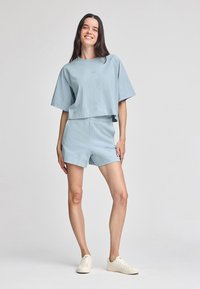 T-shirt corta a maniche corte in cotone azzurro chiaro abbinata a pantaloni corti coordinati. Entrambi presentano una vestibilità comoda e dettagli di cucitura minimi. Sneakers color crema.