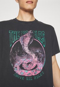 Černé bavlněné tričko s grafikou hada v růžové a zelené barvě s textem "THE KOOPLES" a "ABOVE ALL RULES" v tučném písmu.