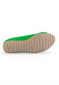 Chaussure plate en suède vert avec une semelle en caoutchouc texturé, présentant un bout arrondi lisse et des détails décoratifs subtils sur le dessus.