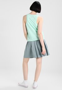 Mintgrön linne i kombination med en veckad knälång kjol i ljusgrått, bärs med vita högtoppar. Slät tygtextur.